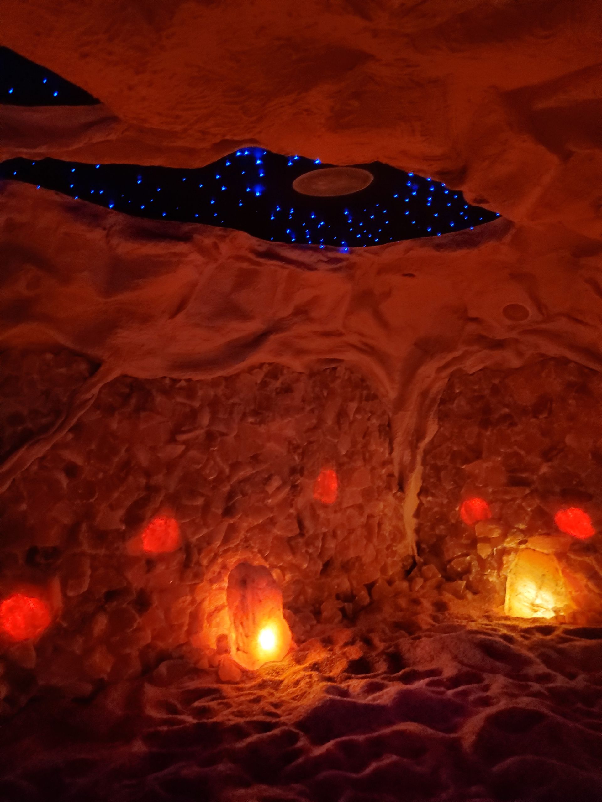 Interior of a snow cave lit with red and orange lights; a starry-night effect is created in the ceiling.