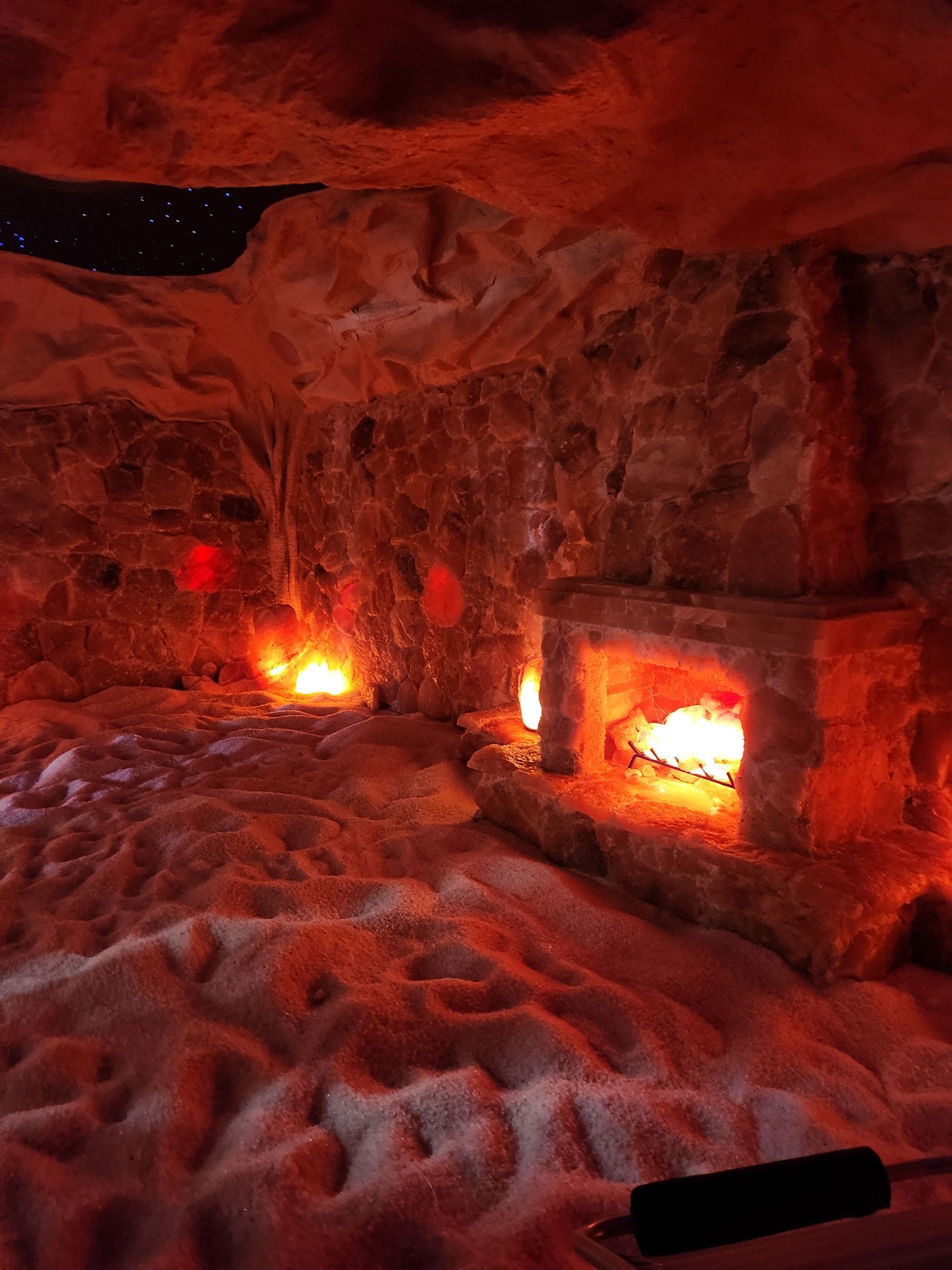 Interior of a salt cave with red lighting, a fireplace, and a snowy floor.