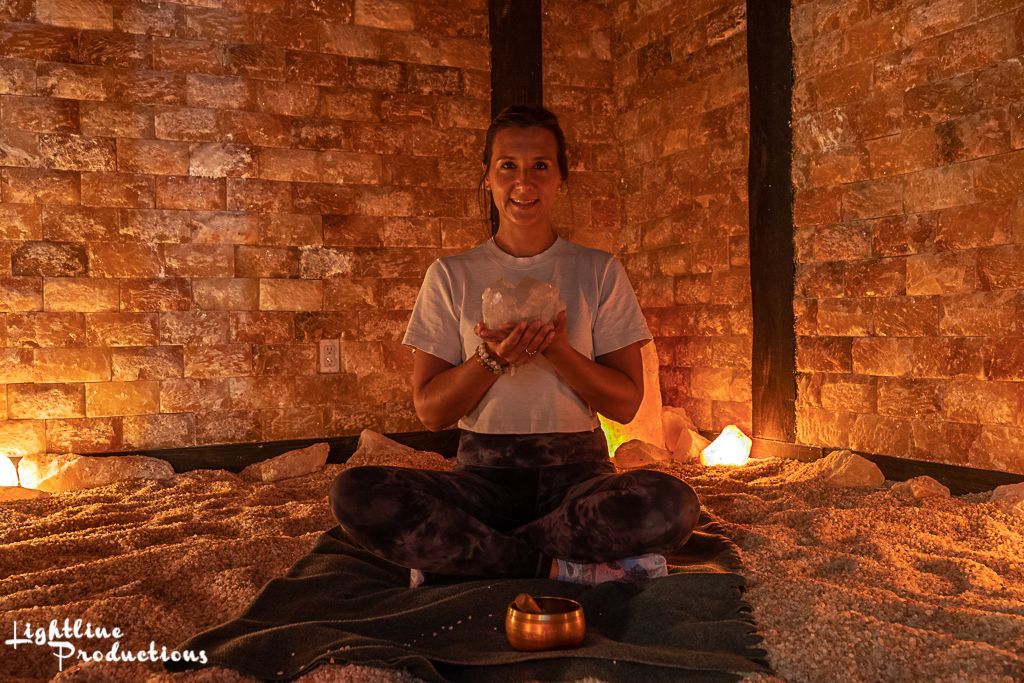 Woman in meditative pose, holding a crystal in a dimly lit salt cave.
