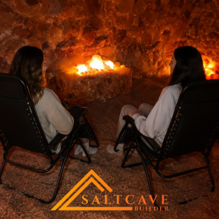 Two people sit in chairs by a glowing fire inside a salt cave.