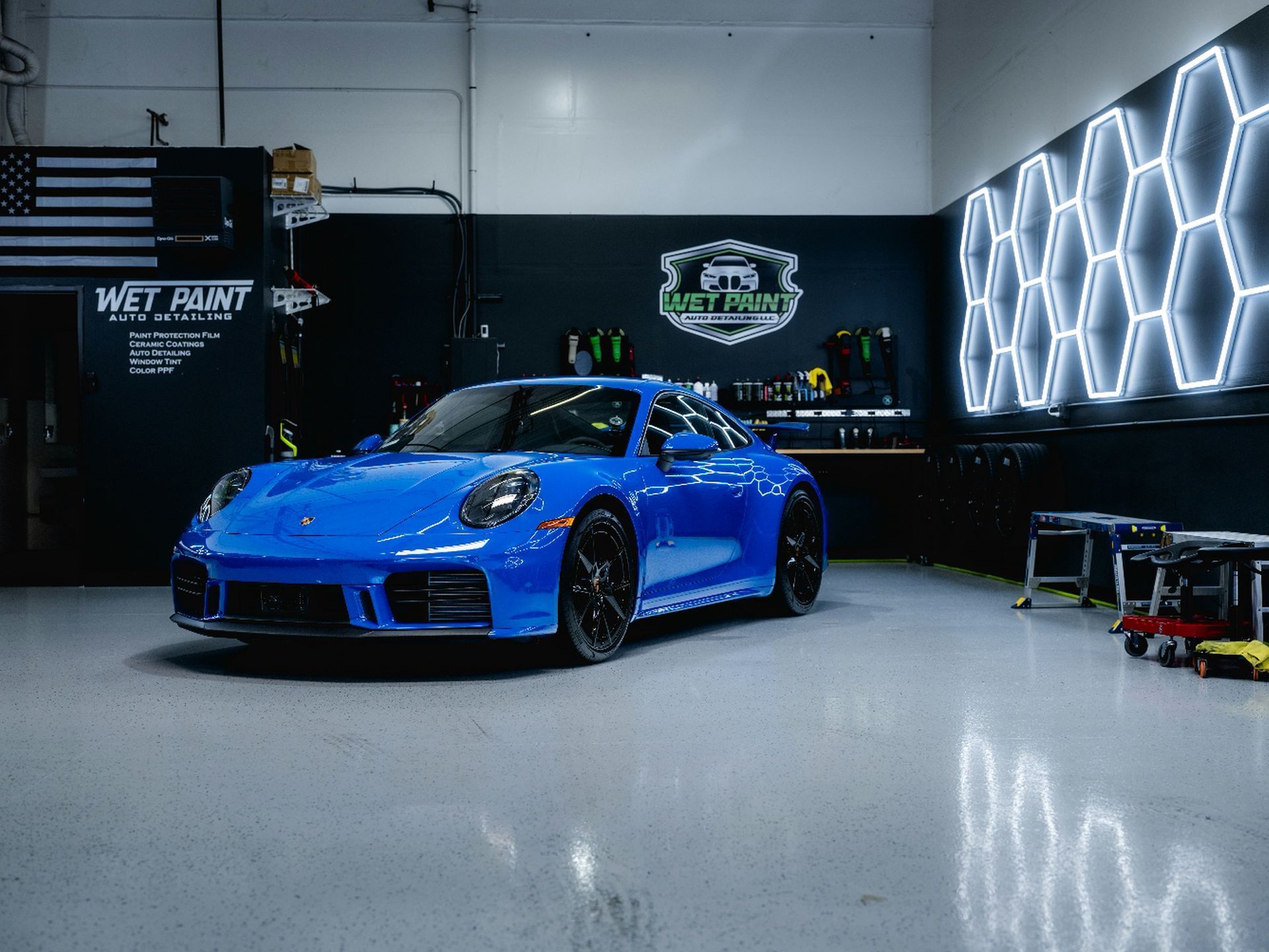 Blue Porsche sports car in a detailing shop, lit by honeycomb-shaped lights.