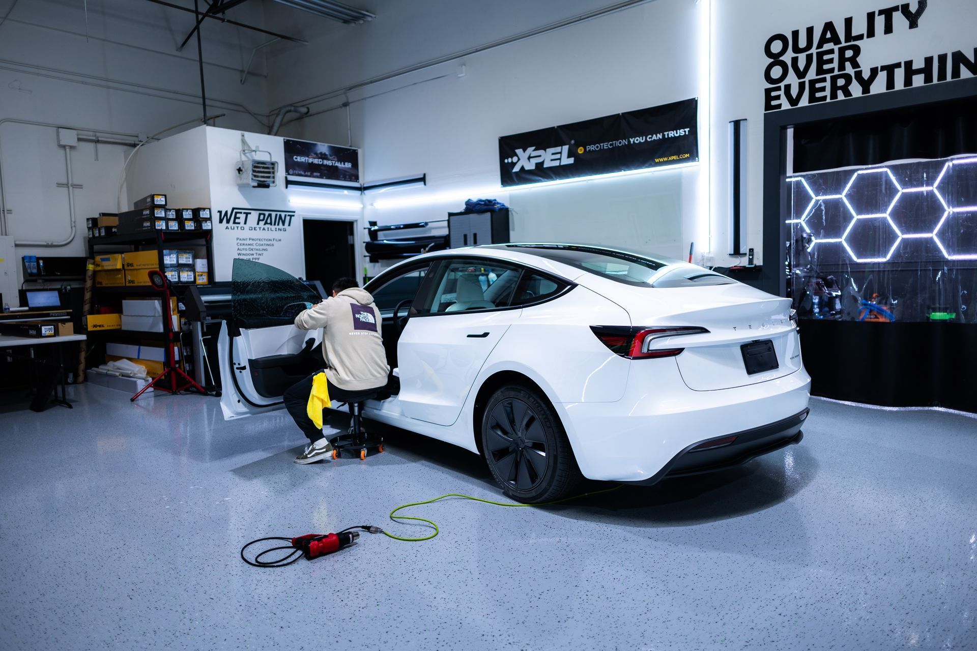A technician works on the interior of a white Tesla in an auto shop featuring neon lighting and signage.