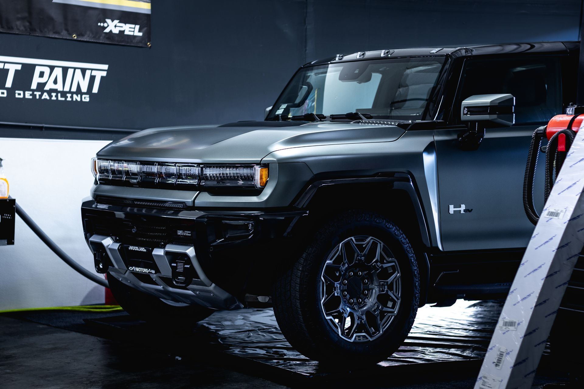 A dark gray Hummer EV parked inside a professional detailing shop with XPEL signage on the wall.