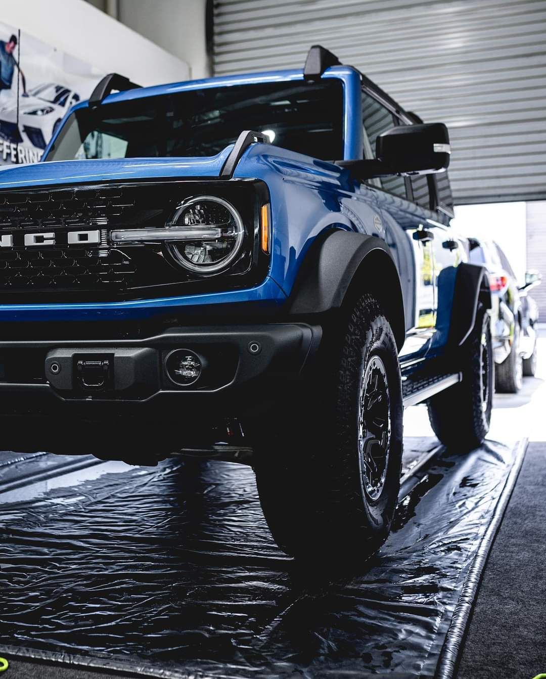 Blue Ford Bronco parked indoors, front view with large tires and off-road styling