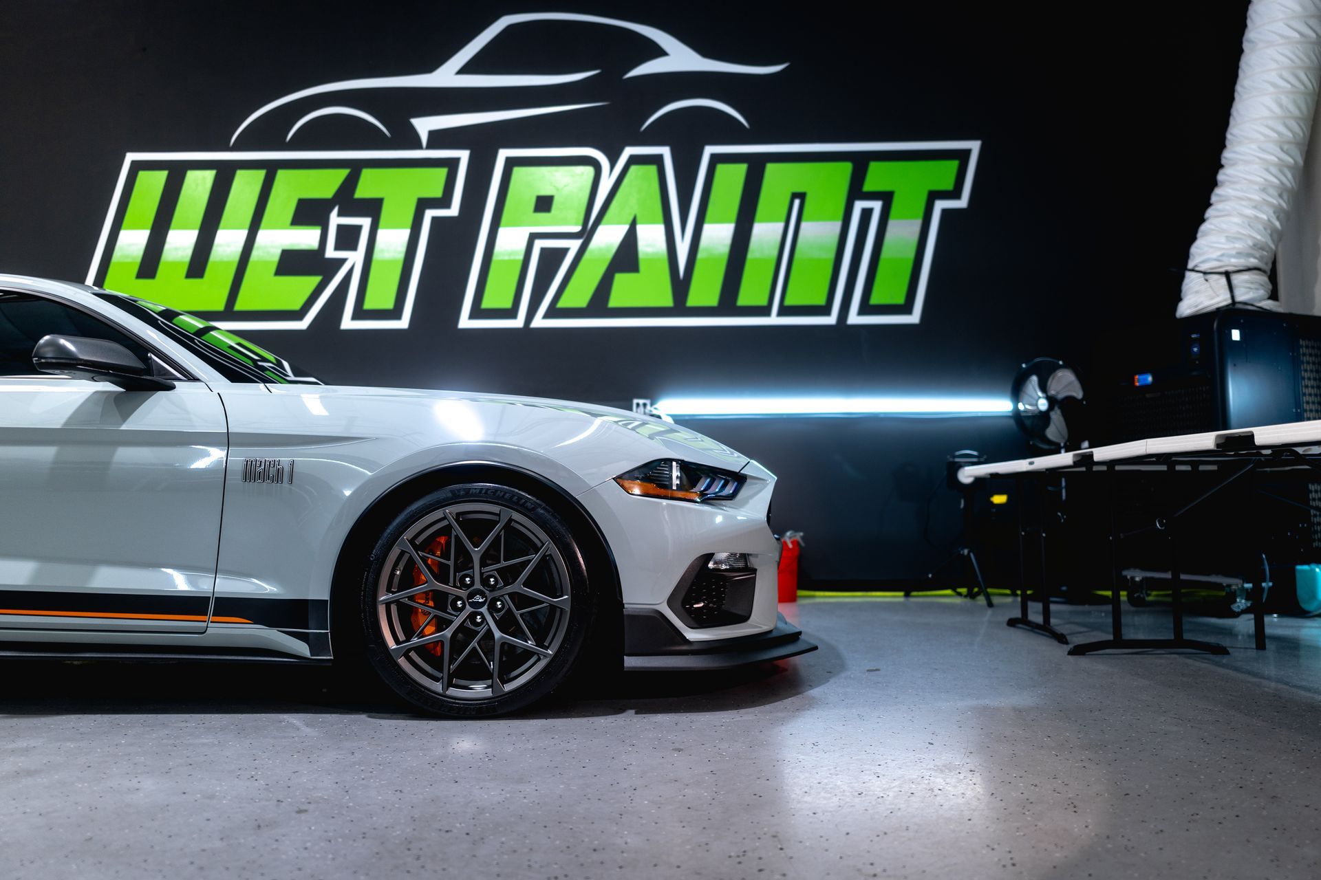 White Ford Mustang Mach-E inside Wet Paint shop. Green and black logo visible.