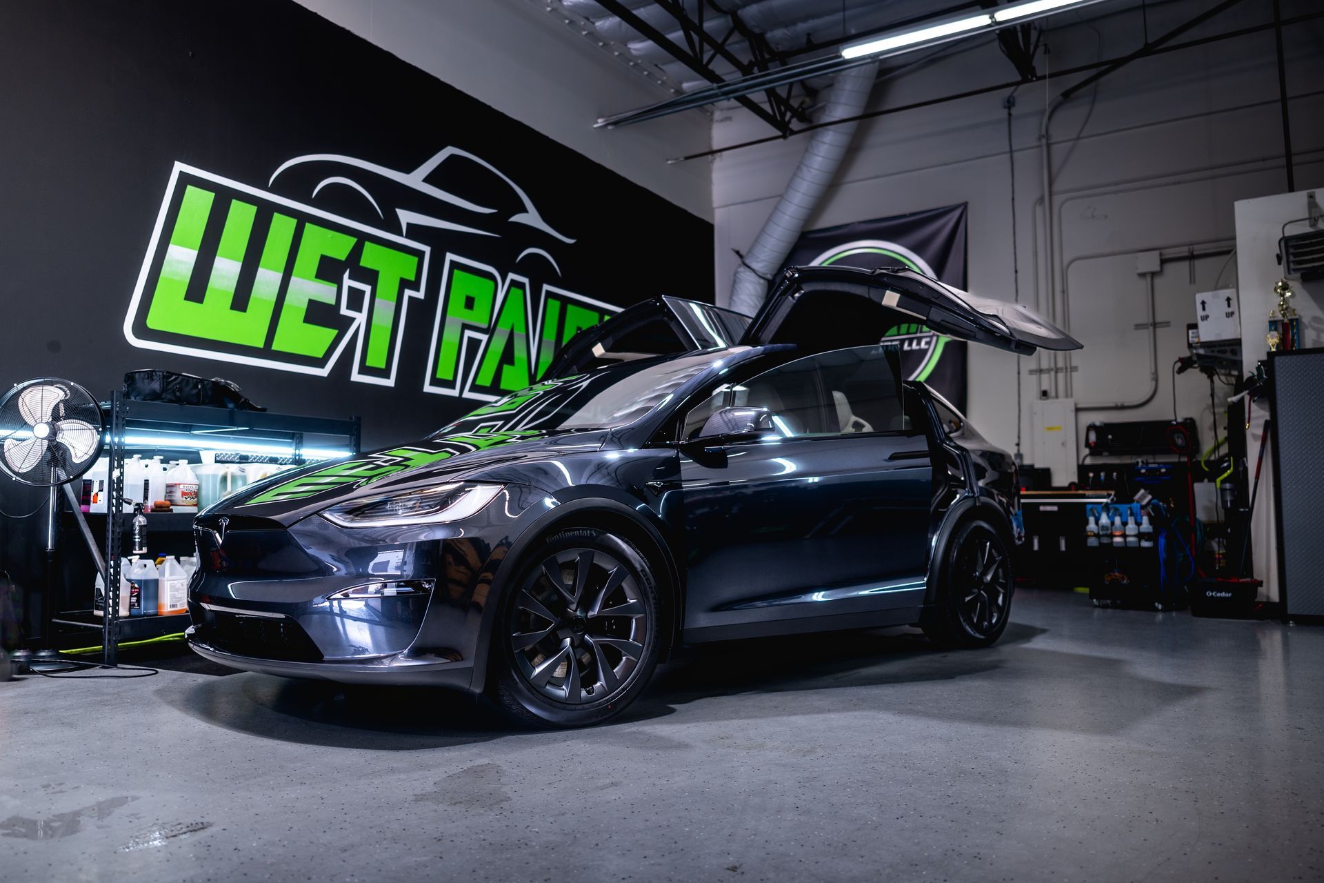 Tesla SUV with gull-wing doors open in a garage.  