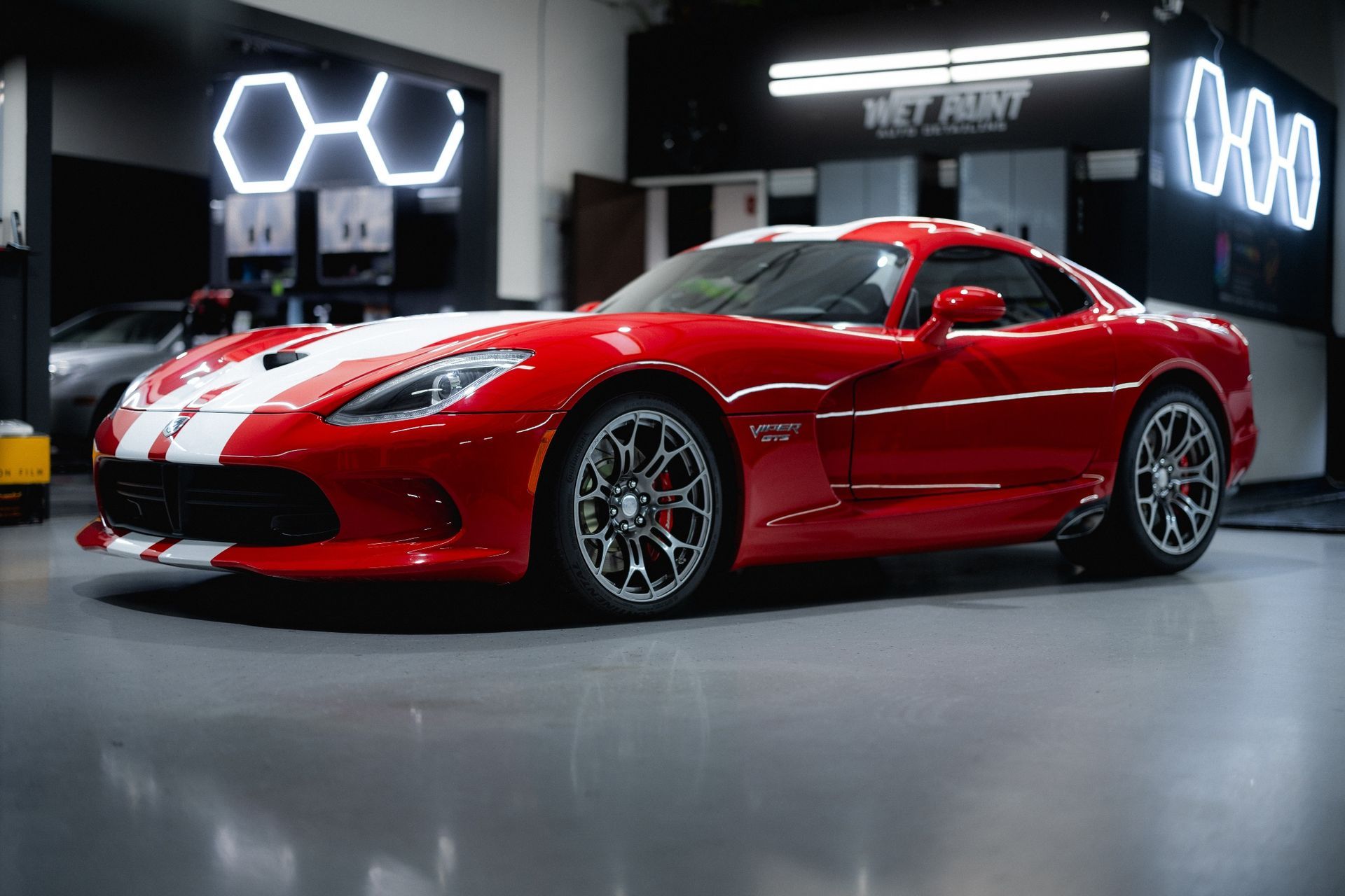 Red Dodge Viper with white racing stripes in a garage.