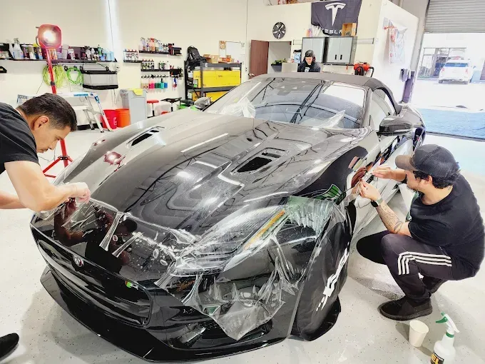 Team installing paint protection film on a black exotic sports car in a detailing studio