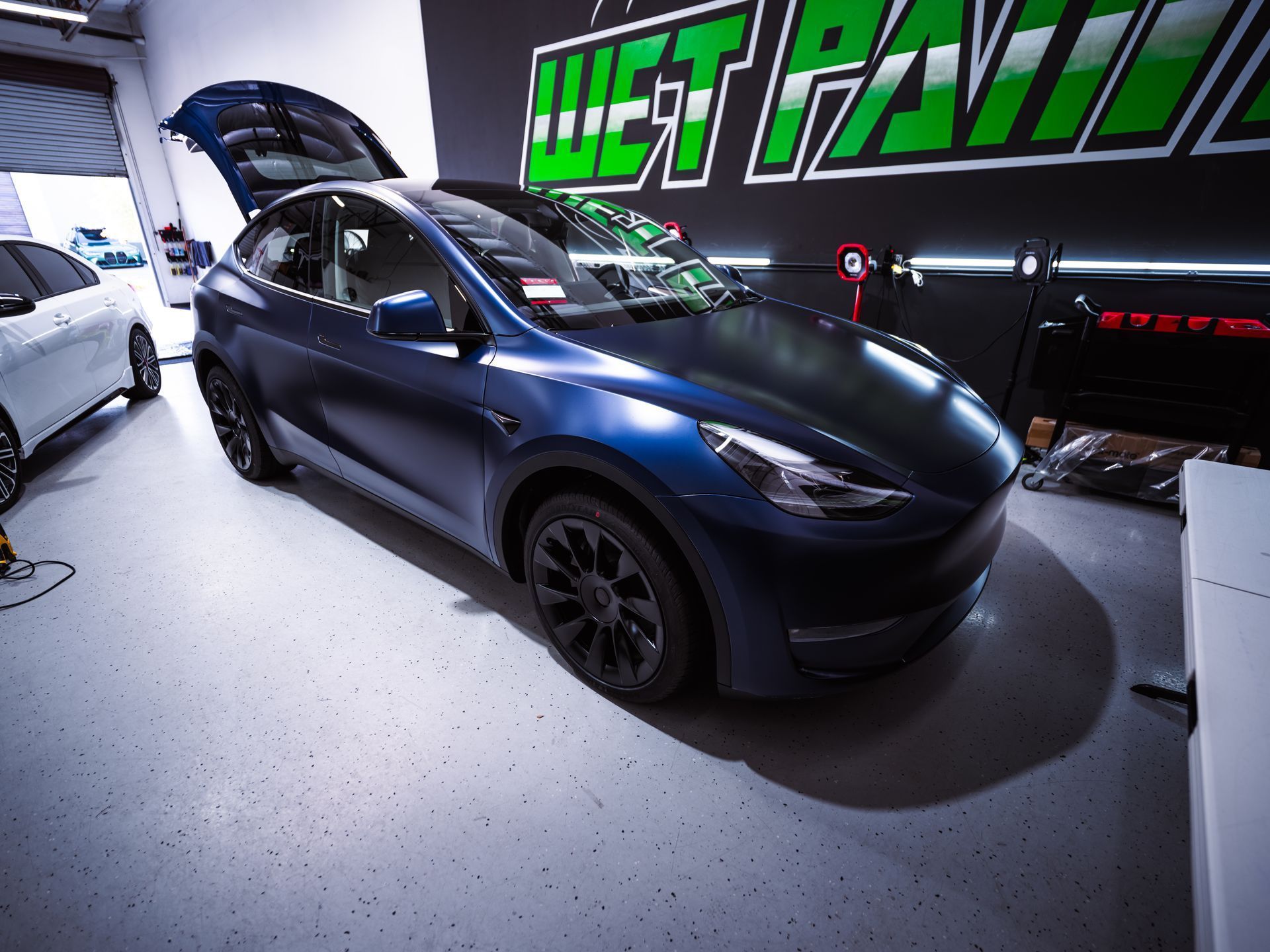 A matte blue Tesla parked inside an automotive shop with the trunk open.