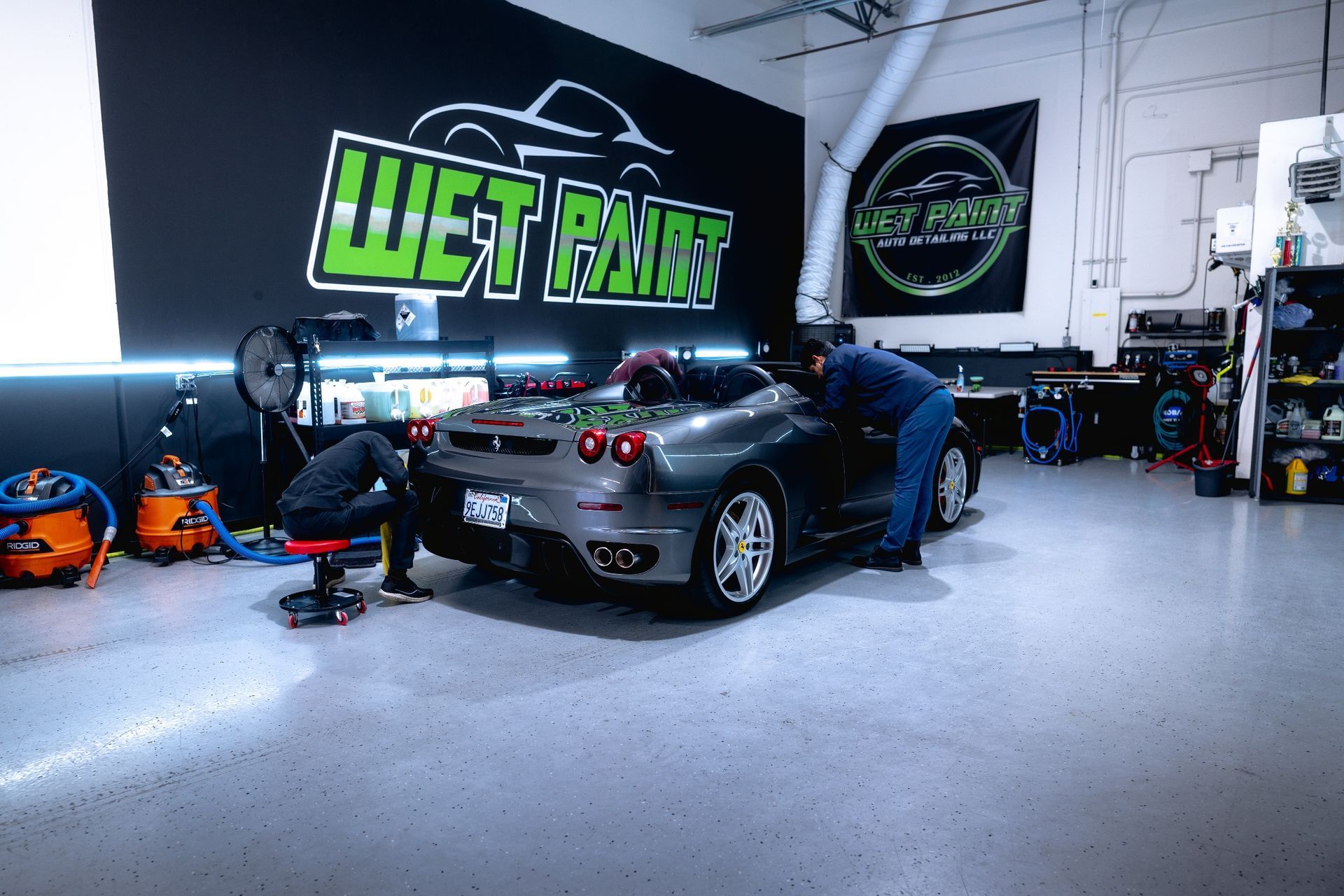 Two people detail a gray Ferrari convertible in a garage with 
