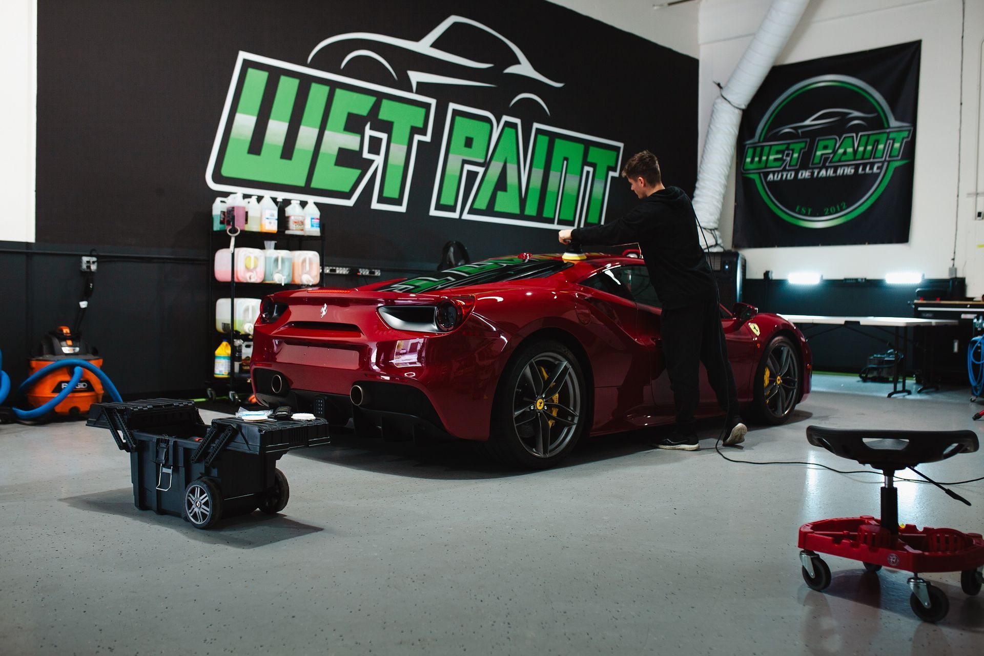 A man is working on a red sports car in a wet paint garage.