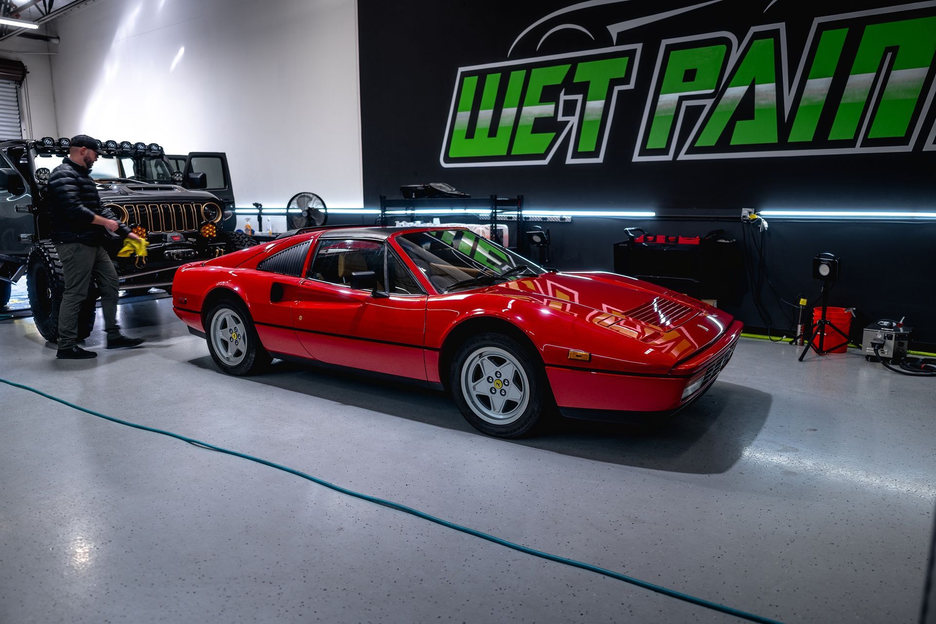 Red Ferrari in a garage, two people nearby, under neon lights.