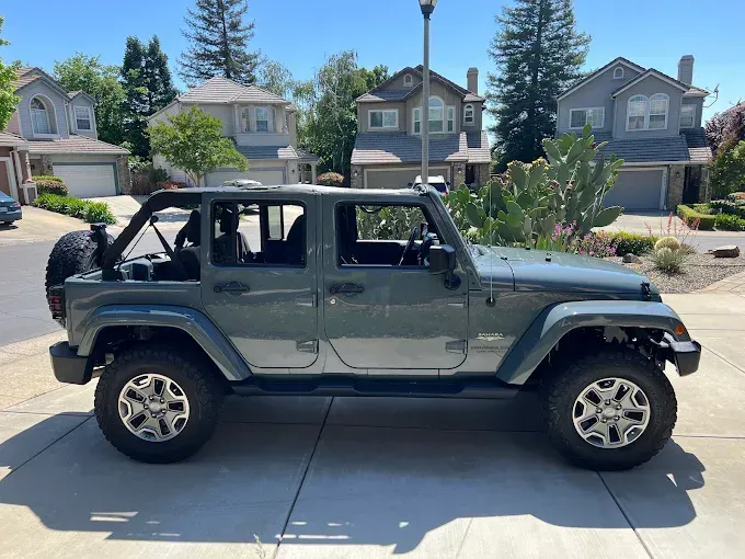 Dark green Jeep Wrangler parked in driveway, freshly coated with ceramic coating for glossy finish.