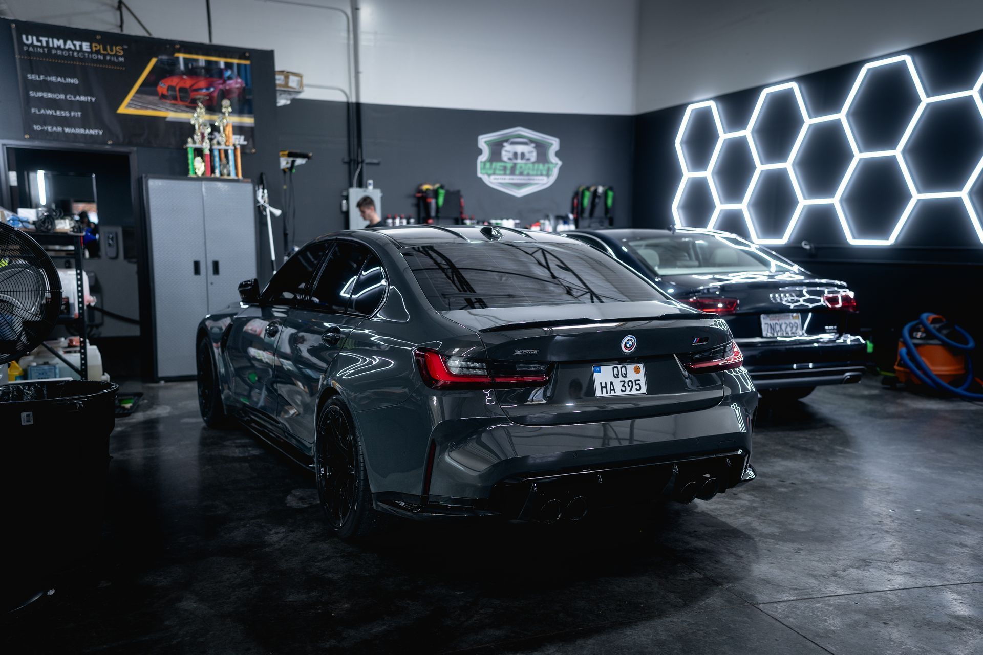 Dark gray BMW and silver Audi inside a detailing garage with hexagon-shaped lights.