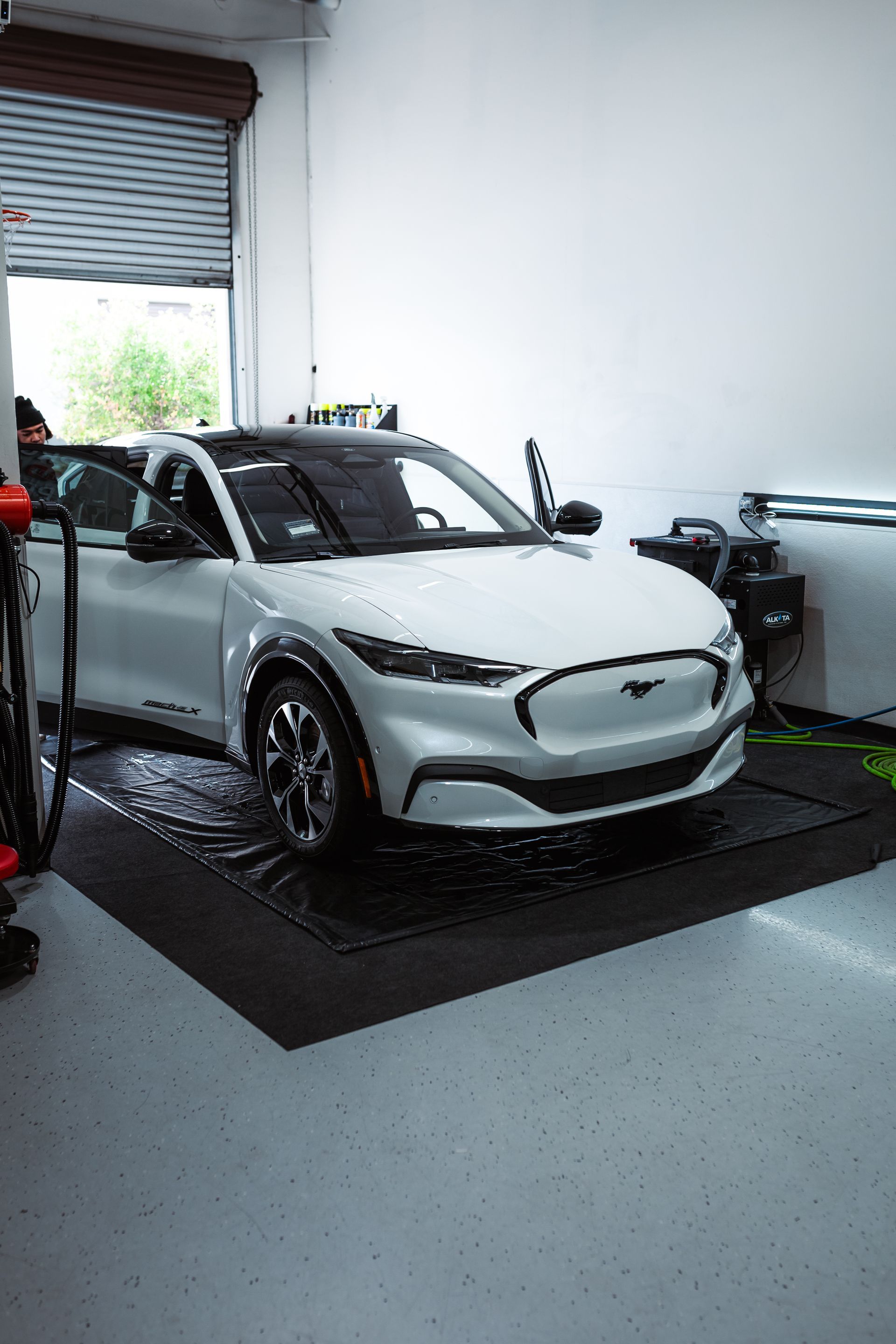 A white Ford Mustang Mach-E electric vehicle parked on a black mat inside a bright garage.