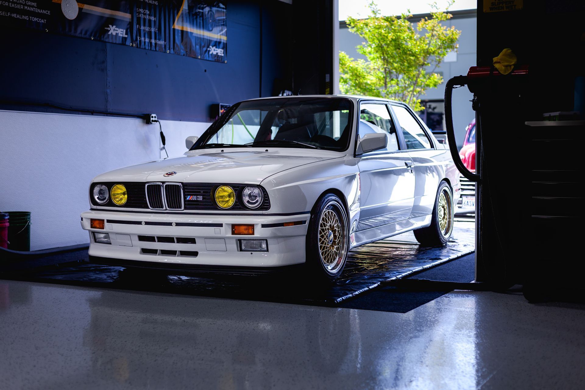 White BMW E30 sports car with yellow headlights parked in a garage.