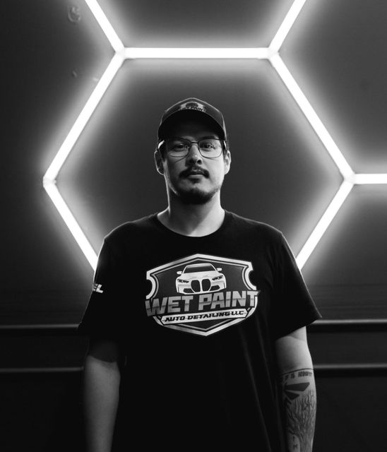 A man wearing a wet paint shirt is standing in front of a neon sign.