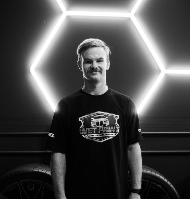 A man is standing in front of a car in a black and white photo.