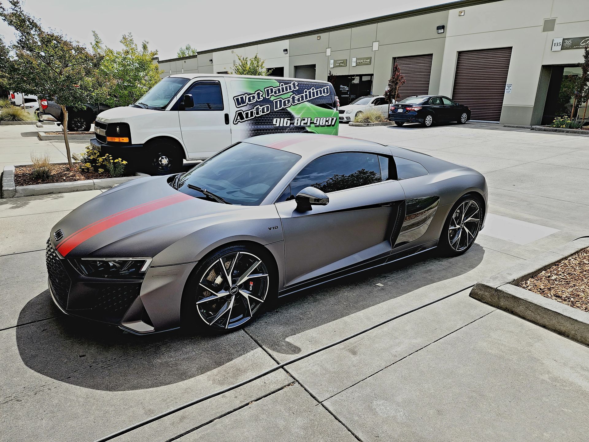 A gray sports car with a red stripe on the side is parked in a parking lot.