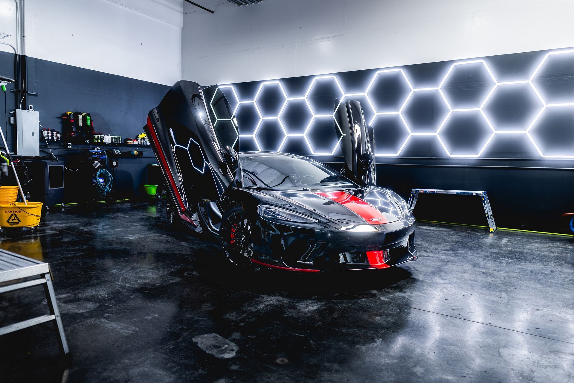Black sports car with doors open in a garage, red accents, hexagon wall lights.