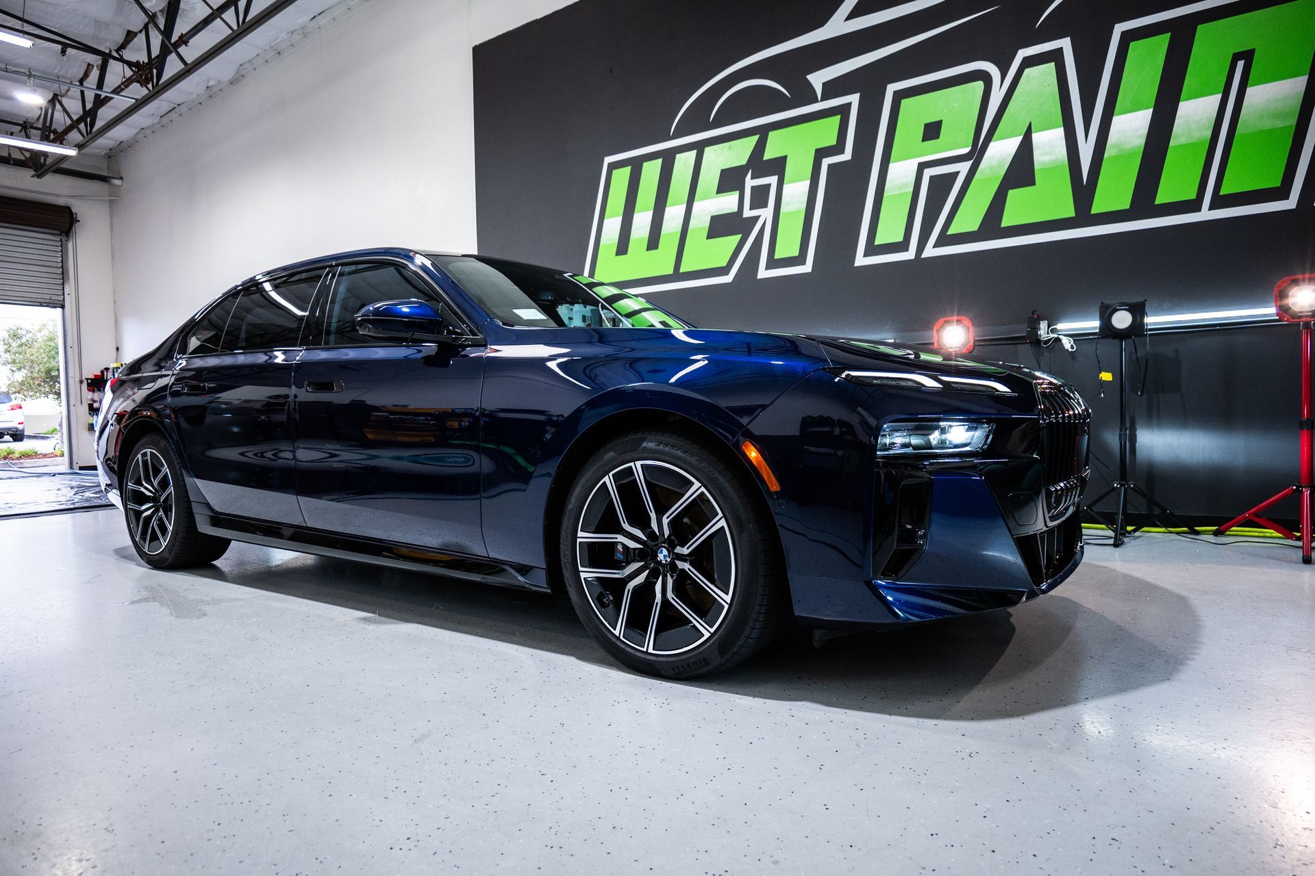 A blue car is parked in front of a wet paint sign.
