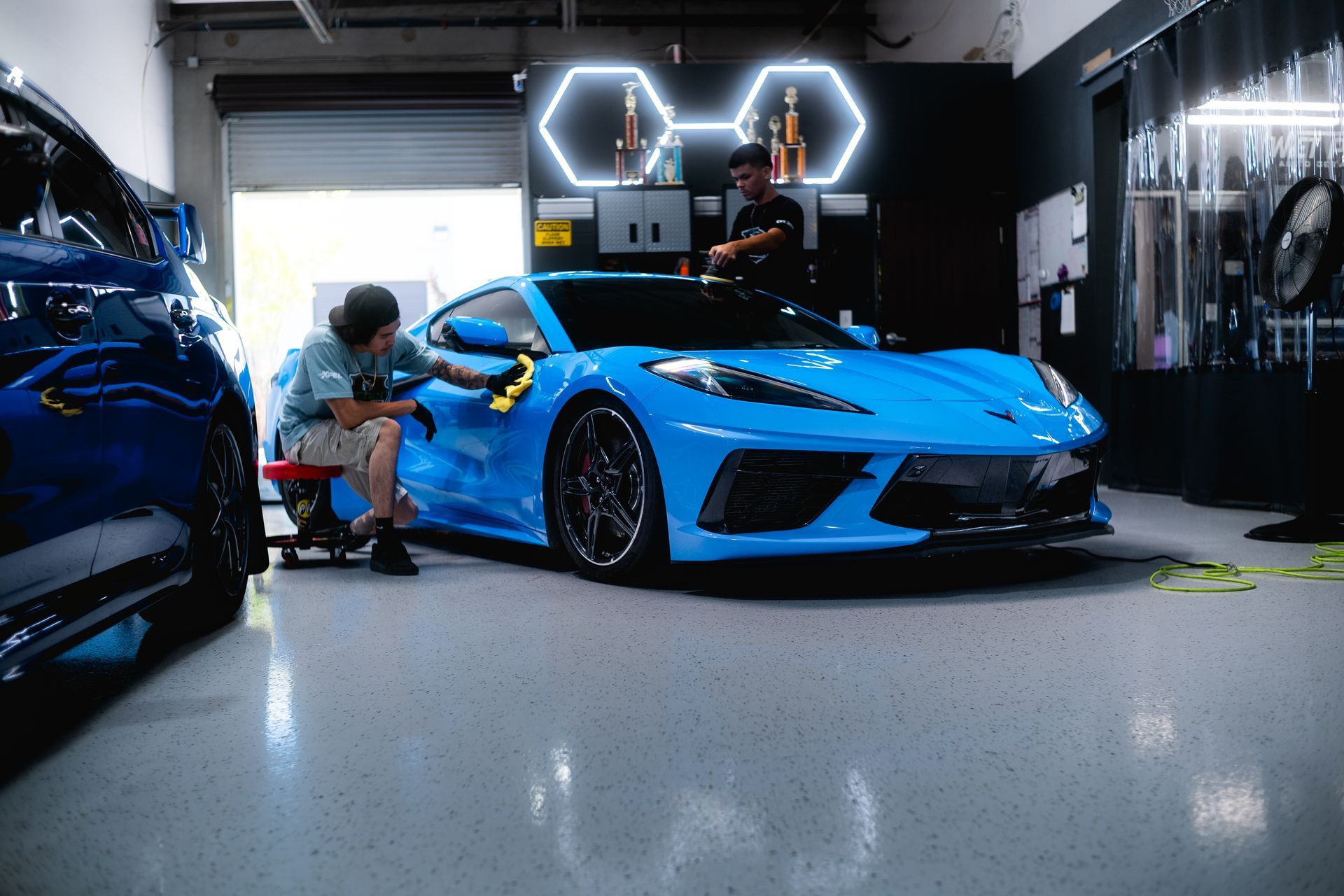 Two people detailing a bright blue sports car in a garage.