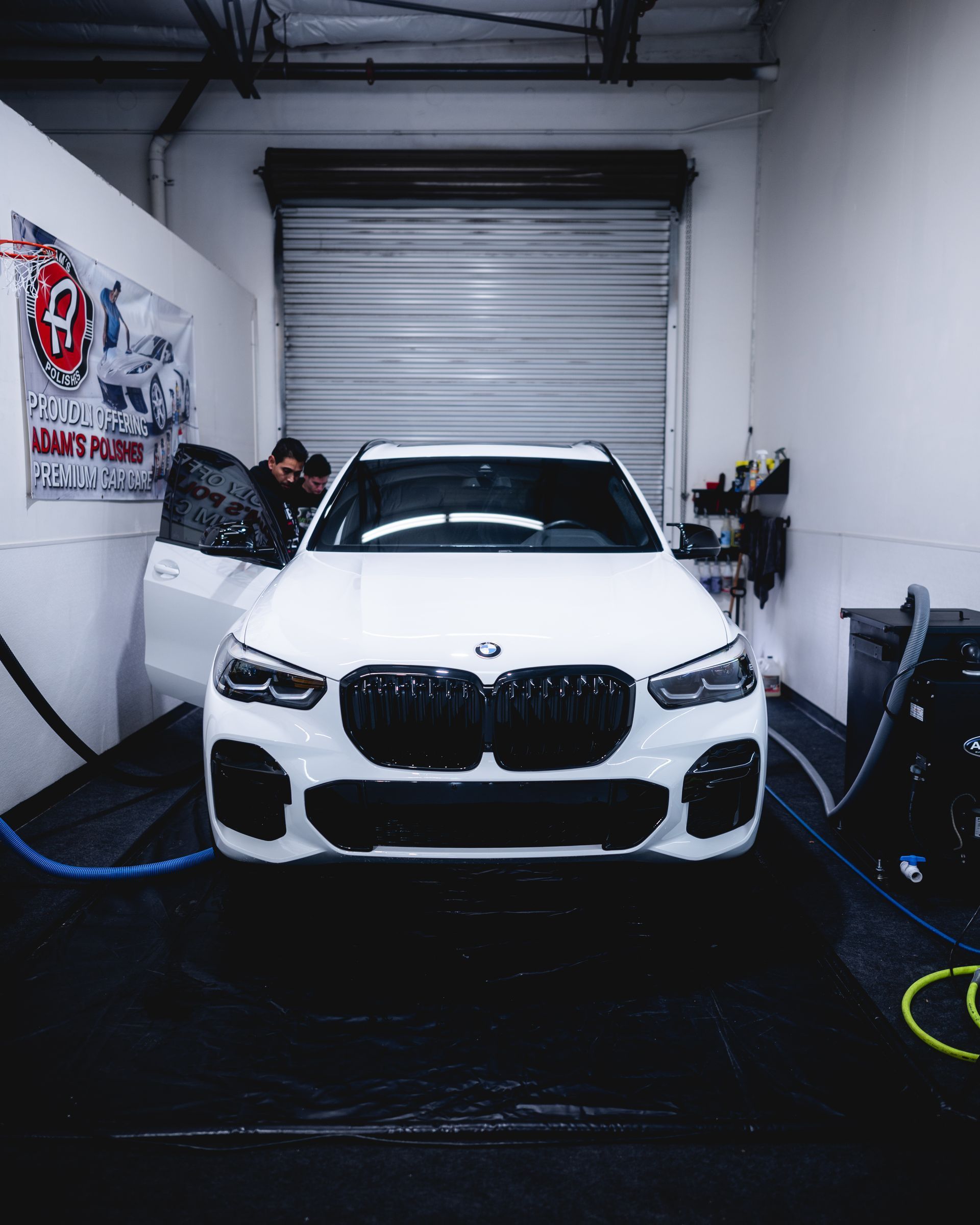 White BMW SUV inside a garage, door open, being worked on.