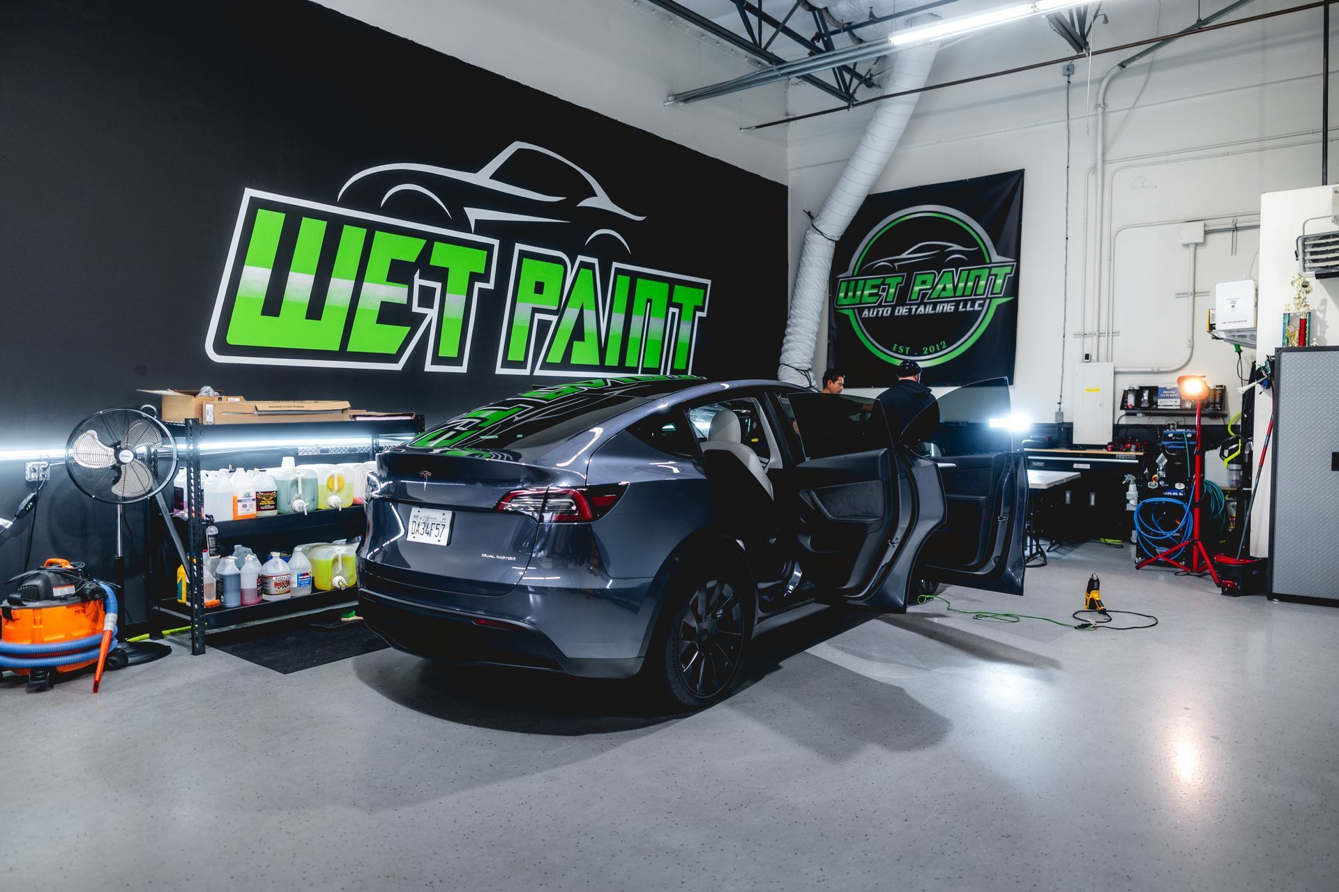 A gray Tesla parked inside a vehicle detailing shop with a 