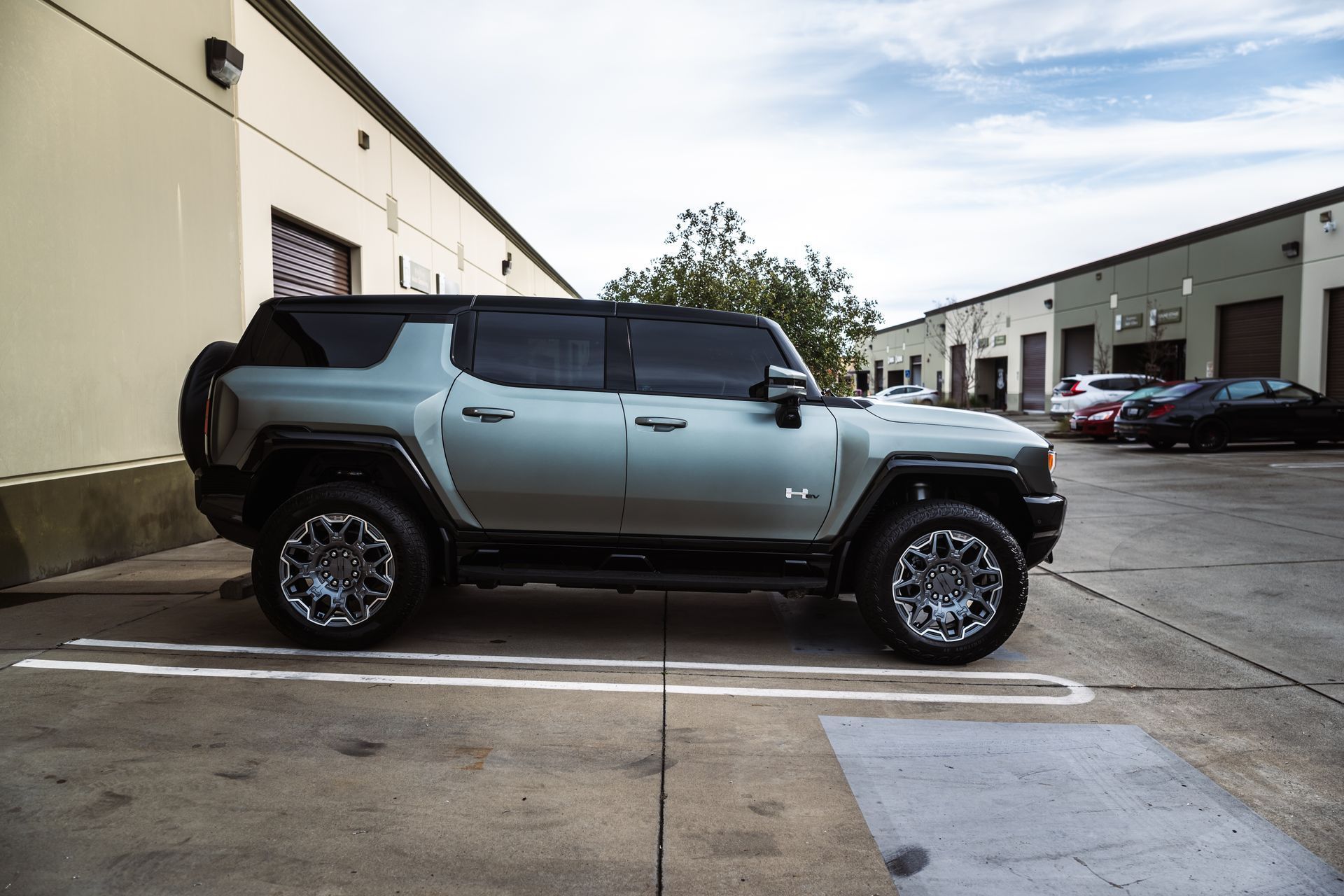 A light green GMC Hummer EV SUV parked on the side of a commercial building on a paved lot.