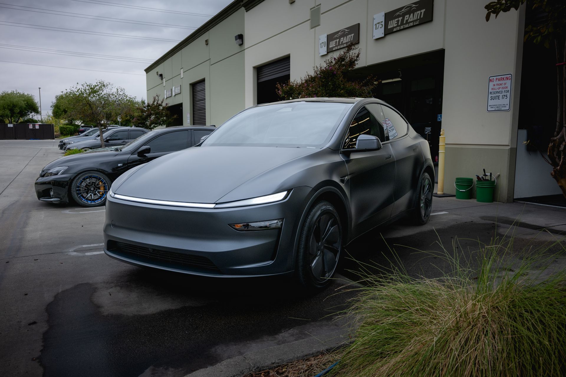 A matte charcoal Tesla parked outside a shop, illuminated by a sleek, horizontal LED light bar across the front.