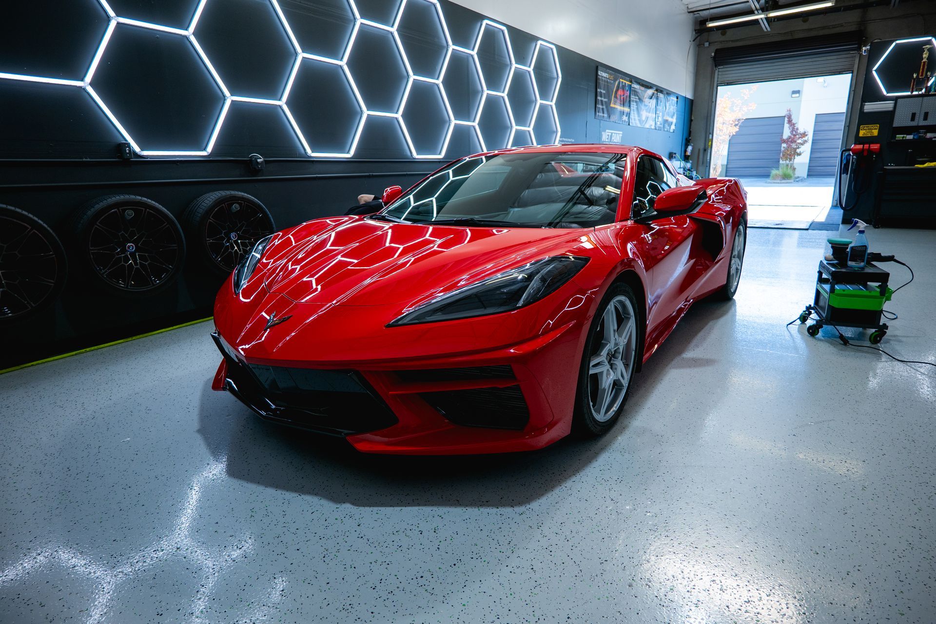 Red sports car parked inside a garage with hexagon-shaped neon lights on the wall.