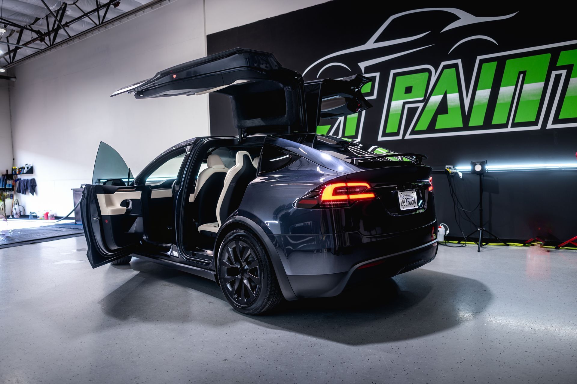 Dark gray Tesla Model X with falcon-wing doors open, parked inside a garage.