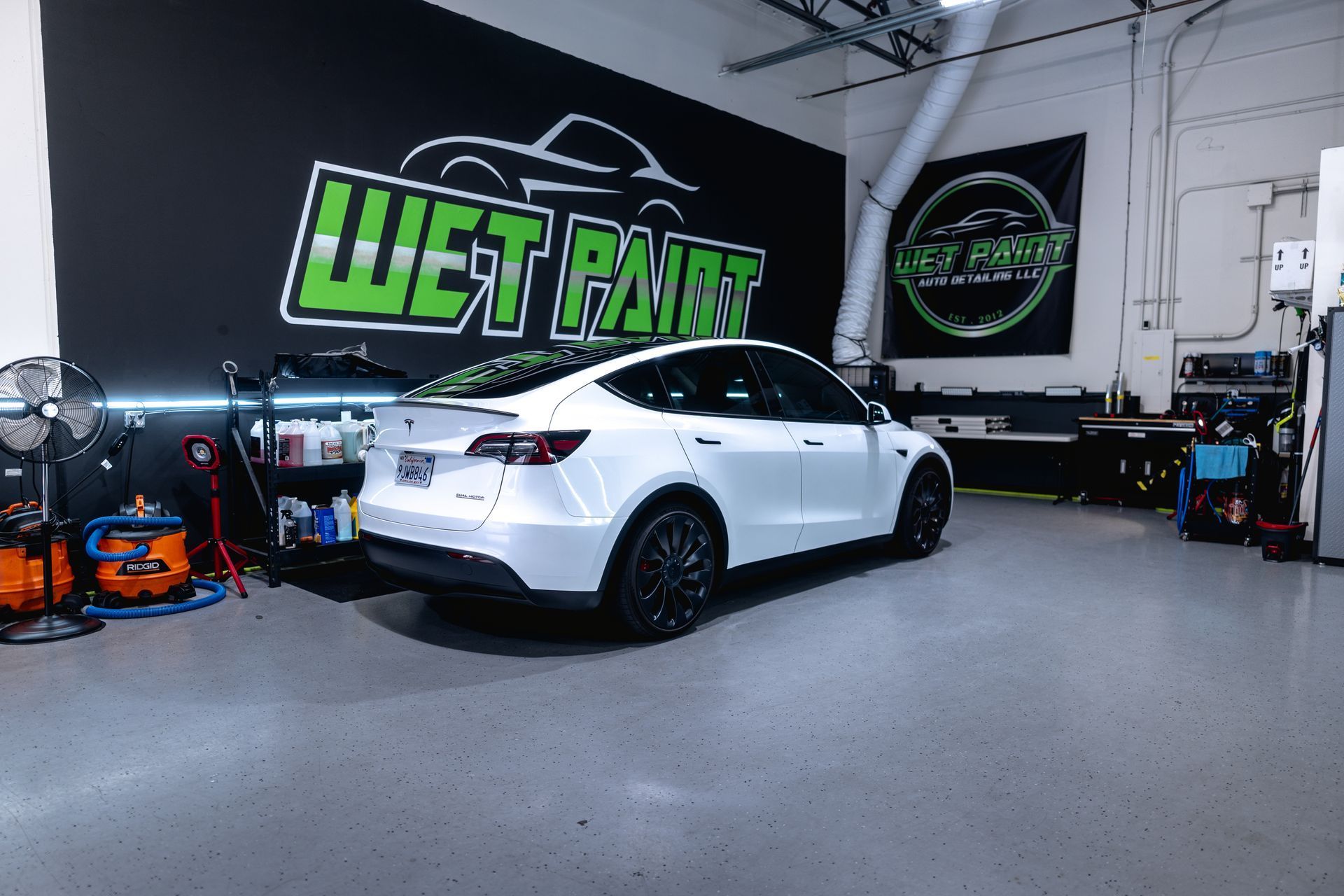 A white Tesla parked in an auto detailing shop with a 