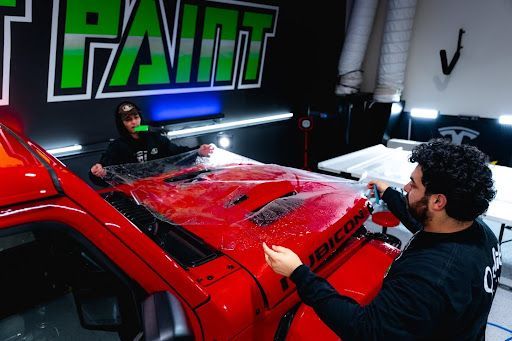 Technicians applying paint protection film on a red sports car in a detailing shop