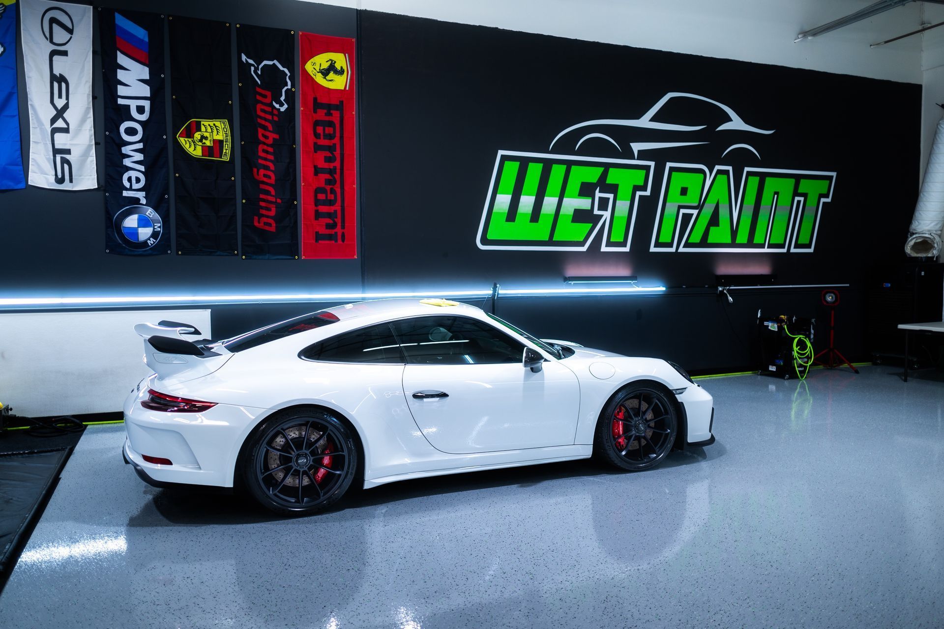 White Porsche sports car inside a garage with car logo on the wall.