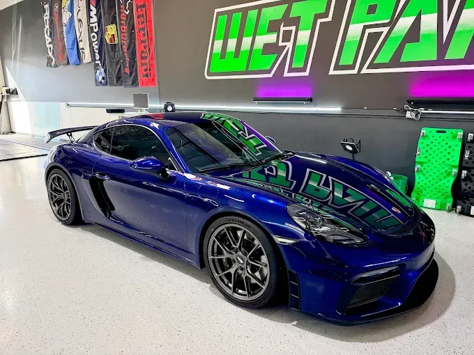 Blue sports car in a showroom with neon wall signage and white flooring