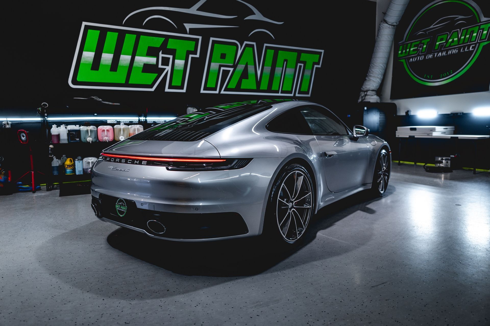 A silver sports car is parked in front of a wet paint sign