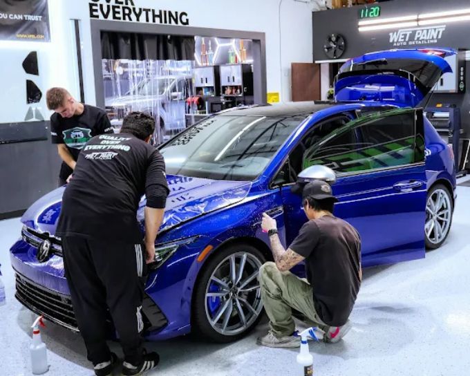 Technicians installing paint protection film on a blue sedan at Wet Paint Auto Detailing