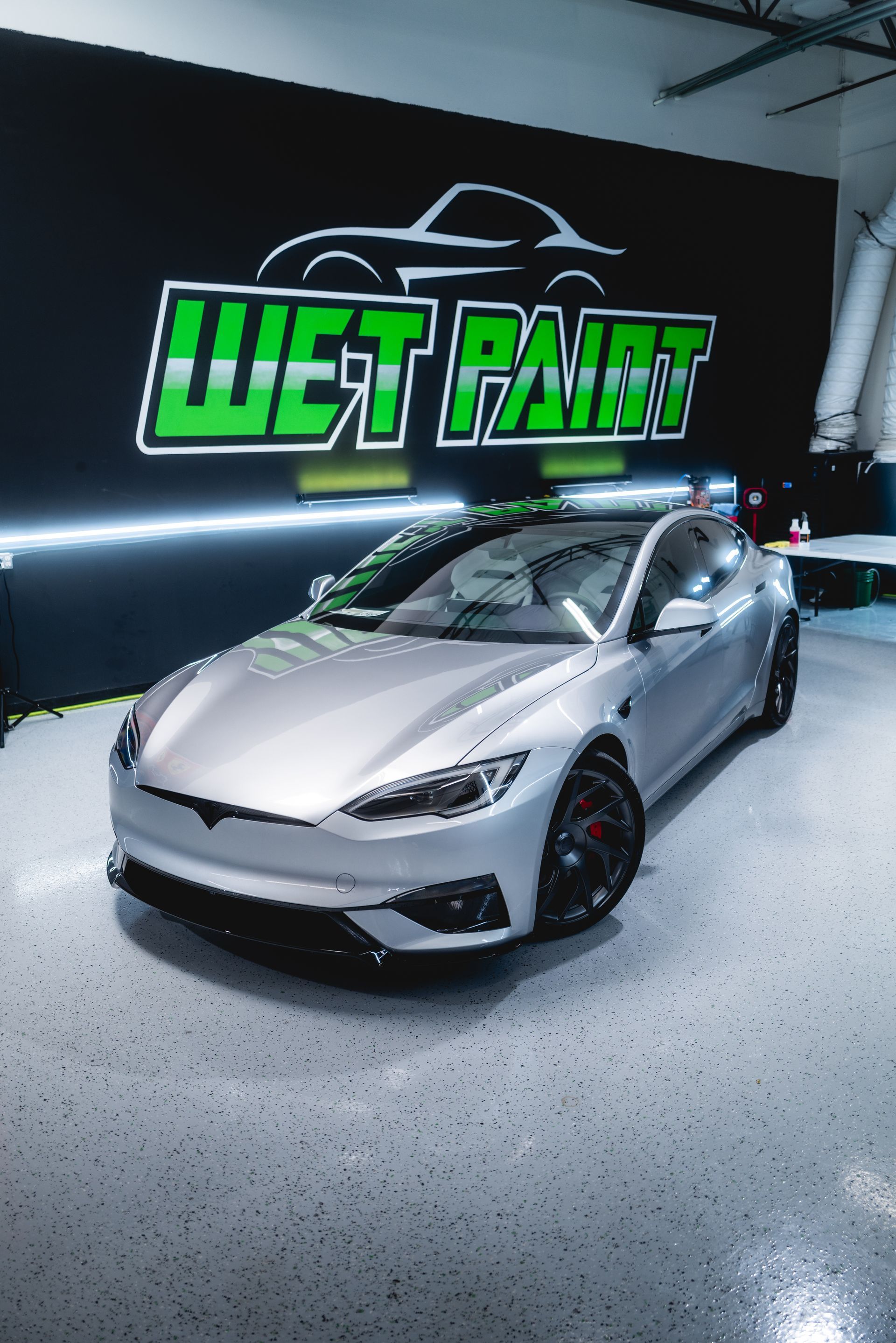 Silver sports car in a bright detailing shop with a neon Wet Paint sign on the wall