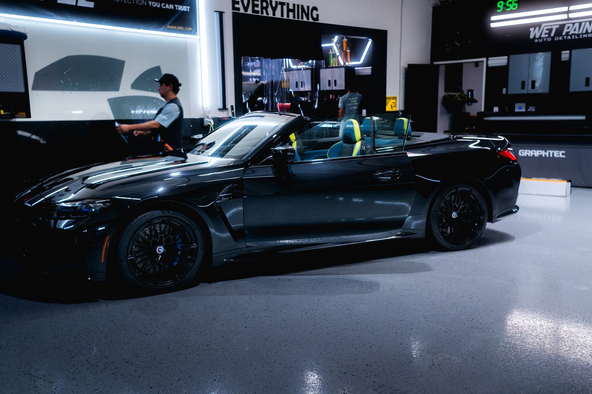 A man is standing next to a black convertible car in a garage.