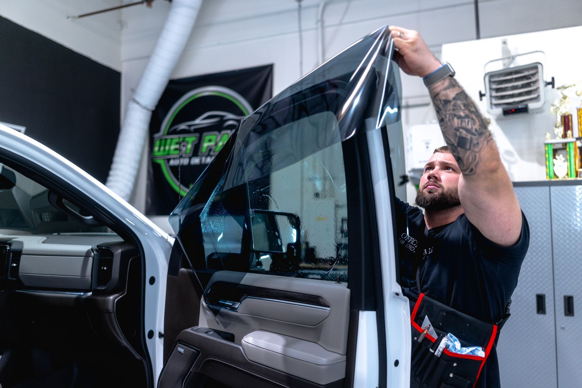 Man applying tint to a car window in a shop. He's holding the dark film.