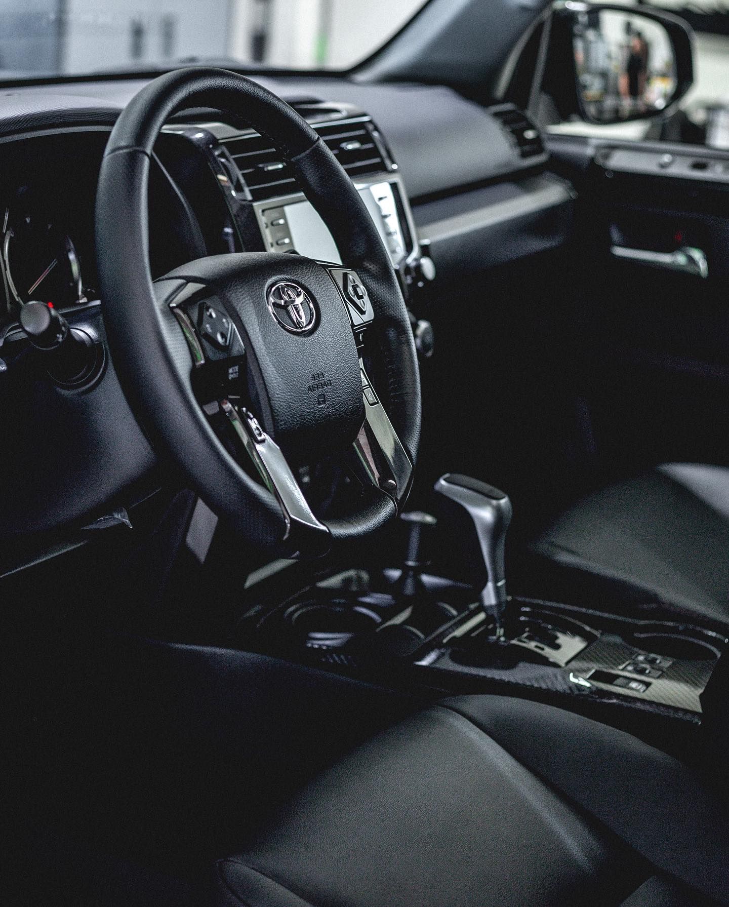 Black car interior with steering wheel, gear shift, and seats. Toyota logo prominent.