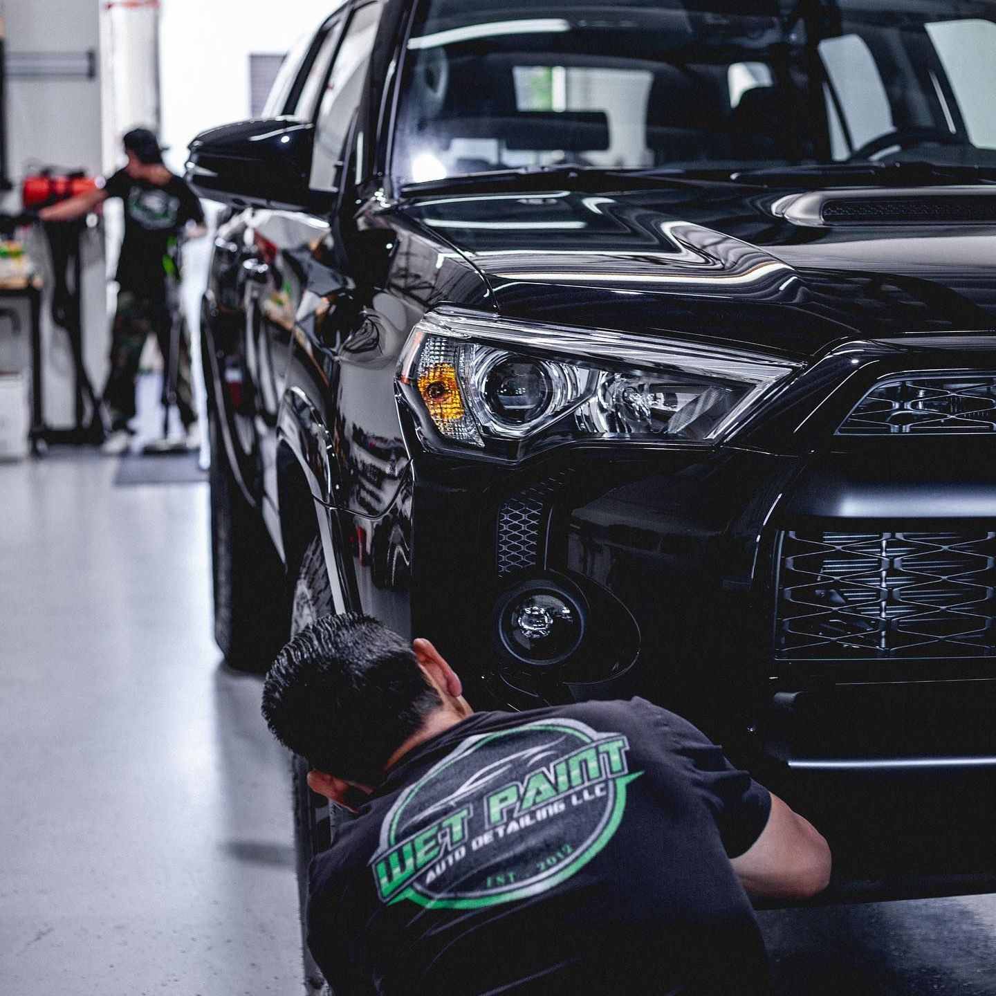Two people working on a black SUV in a detailing shop. One examines a tire.