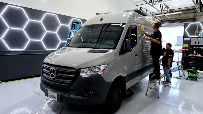 White Sprinter van in a garage, workers applying ceramic coating for glossy protective finish.