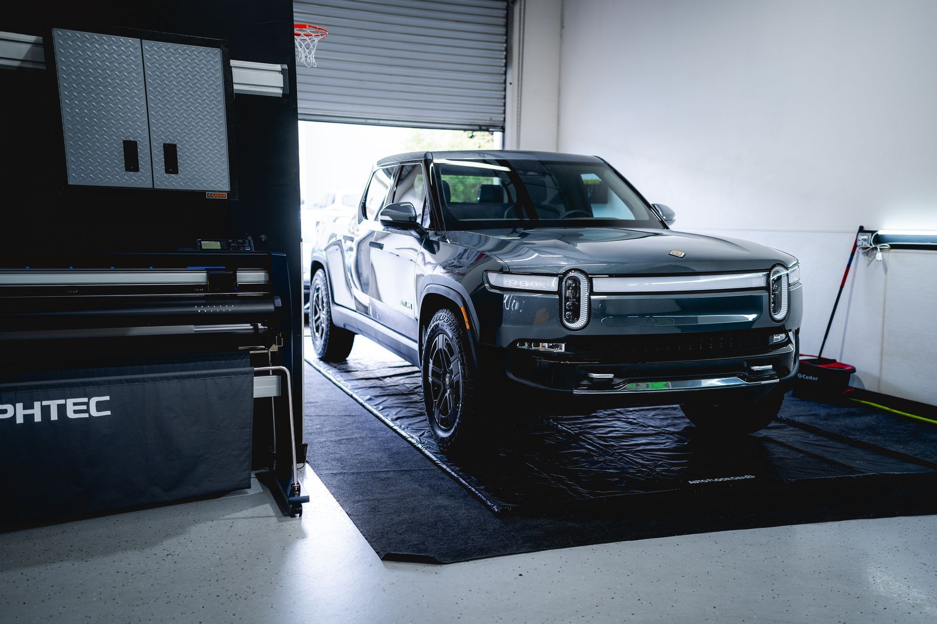A dark gray Rivian electric truck parked inside a bright, clean garage studio.