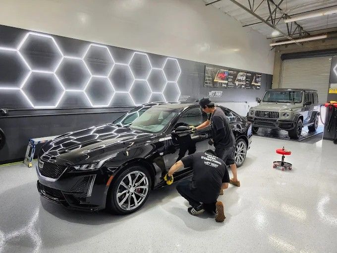 Two Wet Paint technicians applying ceramic coating on a black Cadillac CT5 sedan inside the shop