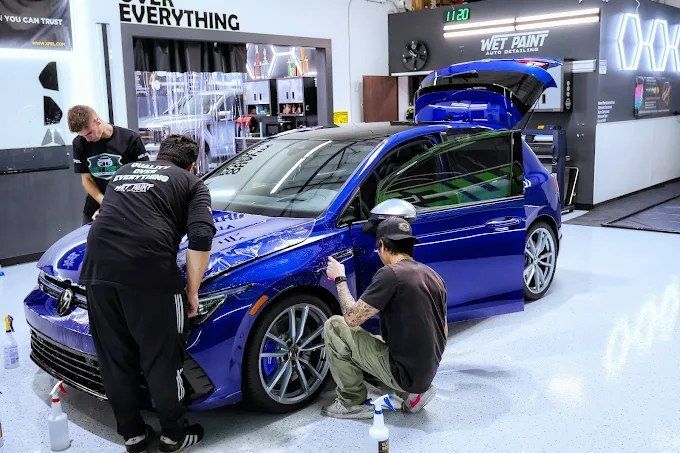 Team of technicians doing PPF installation on a blue Volkswagen Golf R inside Wet Paint detailing shop