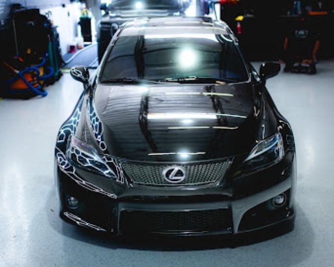 Blacked-out Lexus IS F with custom hood inside shop, showcasing a glossy ceramic coating finish