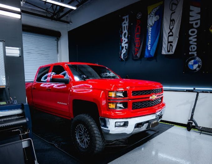 Red lifted Chevy Silverado truck on a dyno inside Wet Paint shop, prepped for ceramic coating service