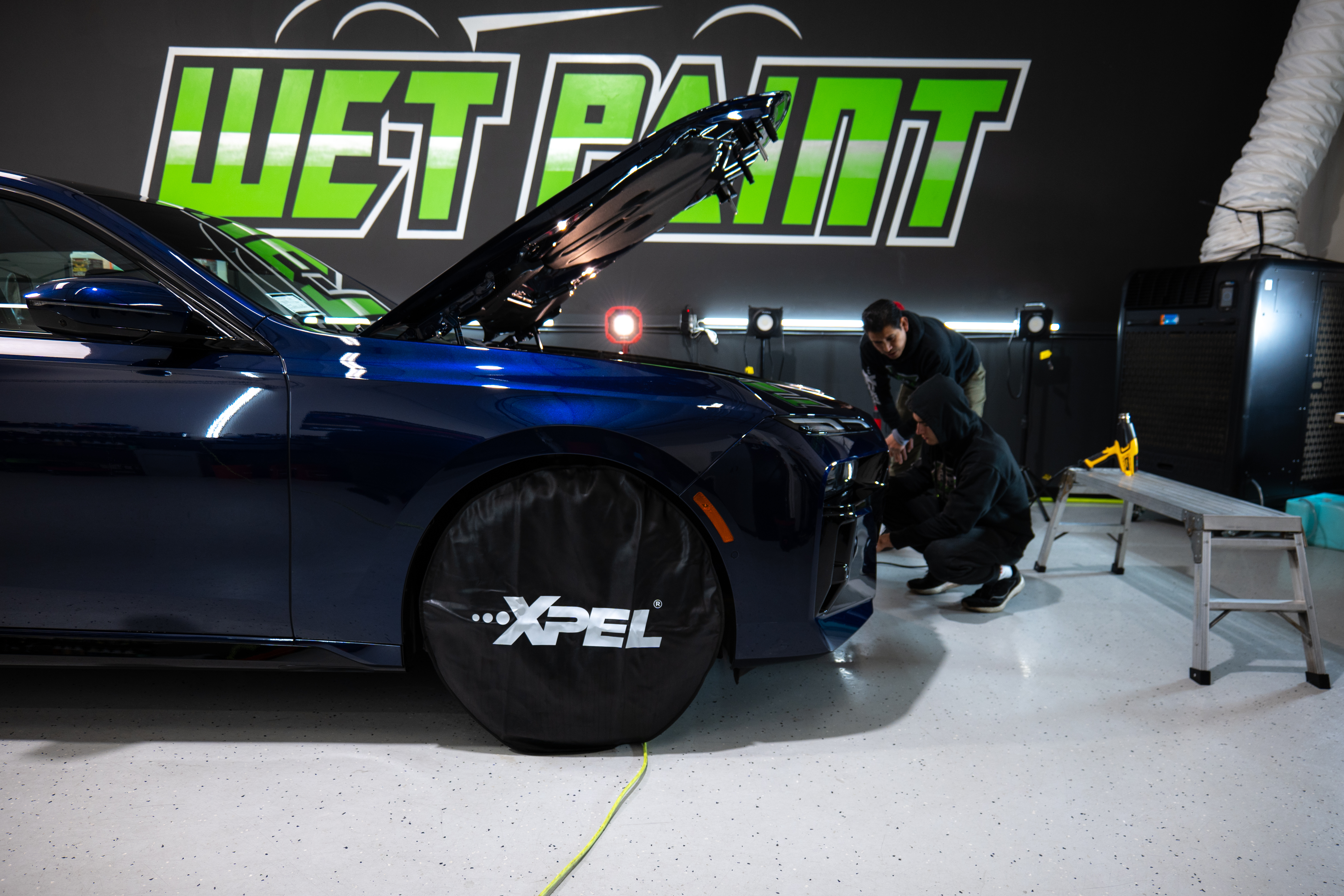 A person is working on a car in a garage with the hood up.